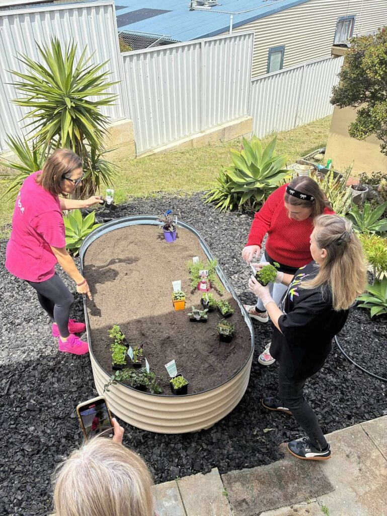 Transition to Independent Living program: OutAbout Oz Programs - three women planting seedlings in raised garden bed
